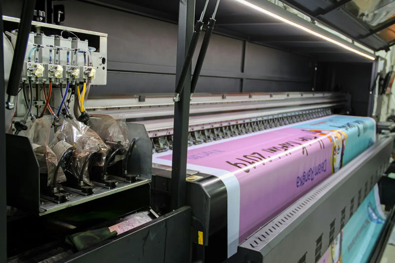 A large industrial printer feeding a long pink banner with printed text