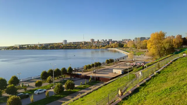 A wide riverfront park with green slopes and trees along a calm blue river